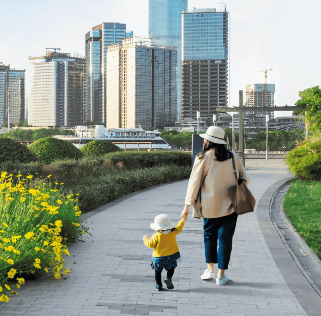 A women walking hand in hand with her young child down a path leading to a city.